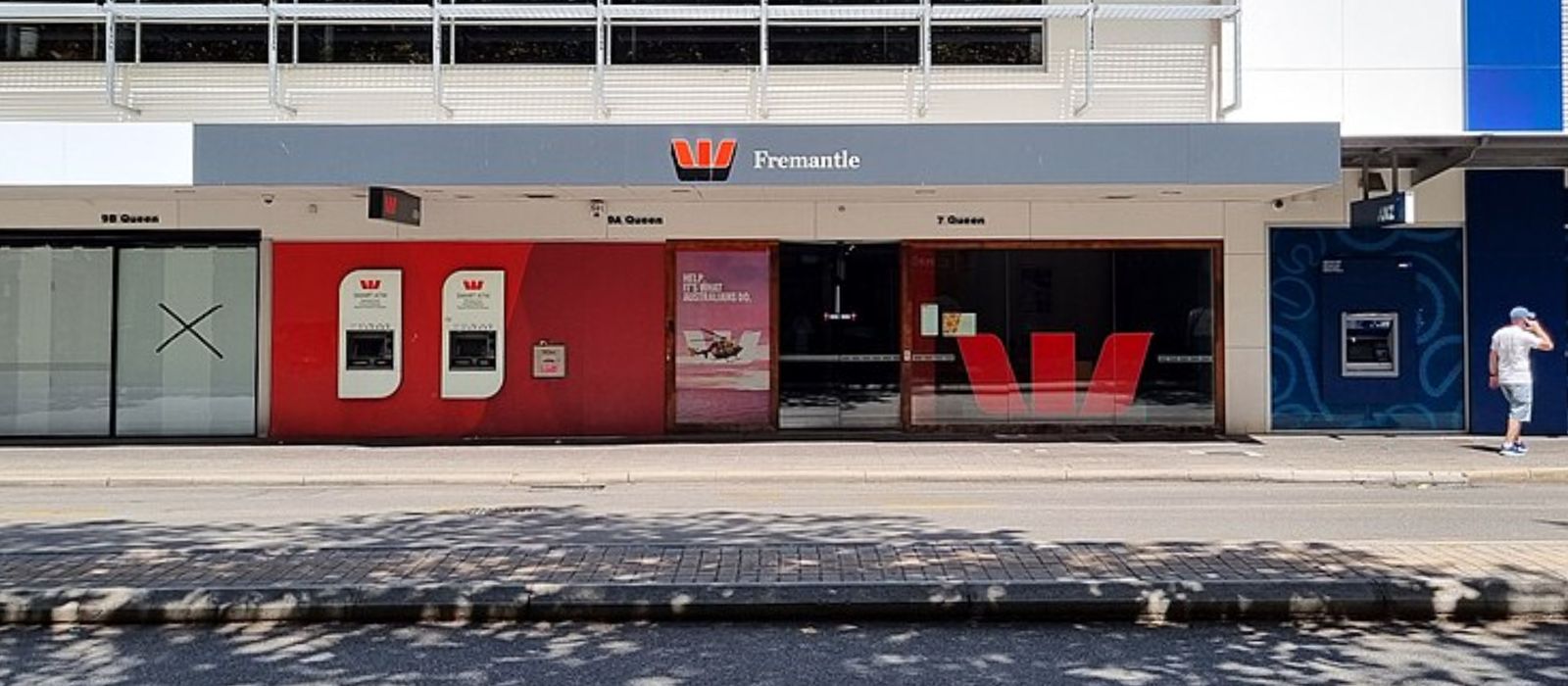 A Westpac branch front in Fremantle, with the Westpac logo above the window and a red wall, seen across a shaded street