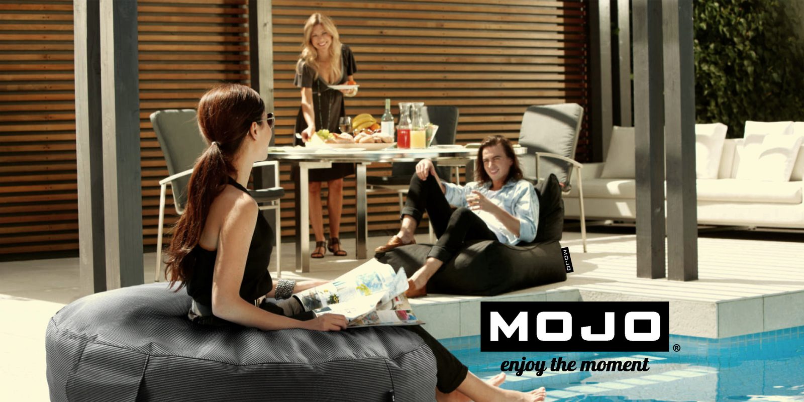 A woman reading on a black Mojo bean bag beside a pool